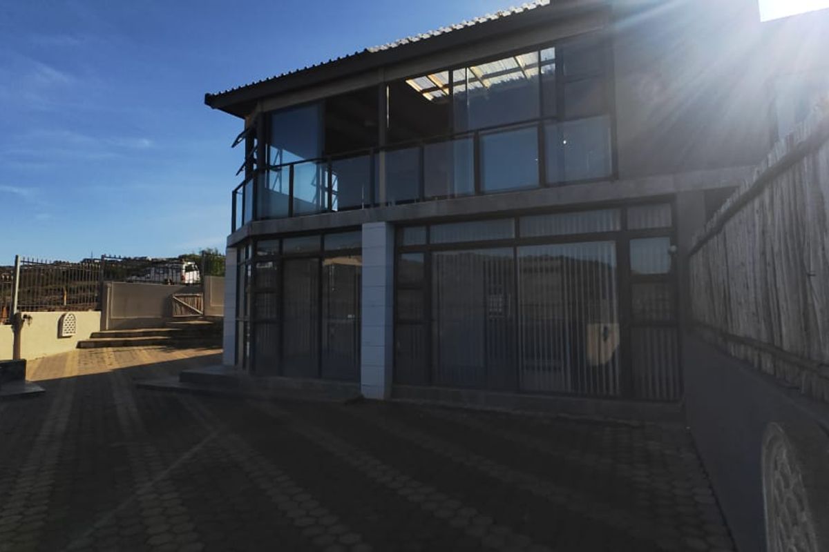 Rear exterior view of the property featuring a paved driveway, a balcony with metal railings, and large sliding glass doors.