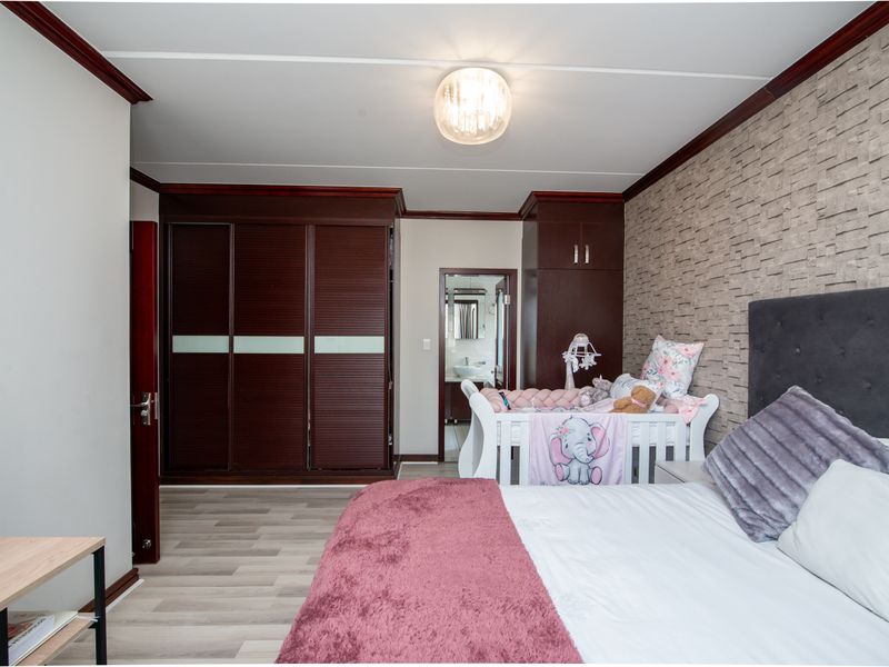 A well-maintained bedroom featuring built-in dark wood cupboards, a textured feature wall, and modern laminate flooring, with an adjoining en-suite bathroom.