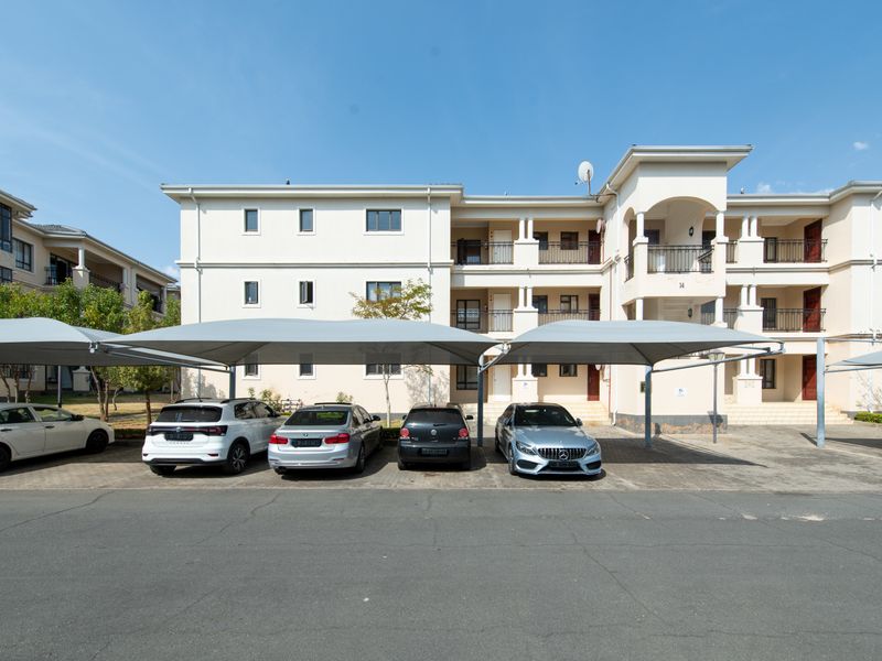 Front elevation of a multi-story apartment complex featuring covered parking bays and paved driveway access.