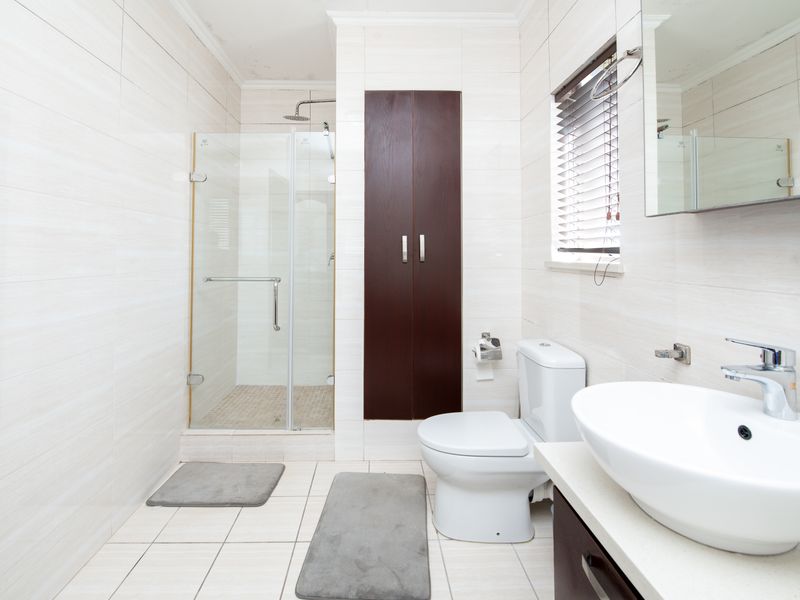 Modern bathroom featuring a glass-enclosed shower, vessel sink vanity, built-in storage cupboard, and neutral tiled finishes throughout.