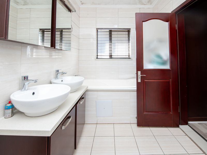 A functional bathroom featuring a double vanity with vessel sinks, a built-in bathtub, and tiled finishes throughout.