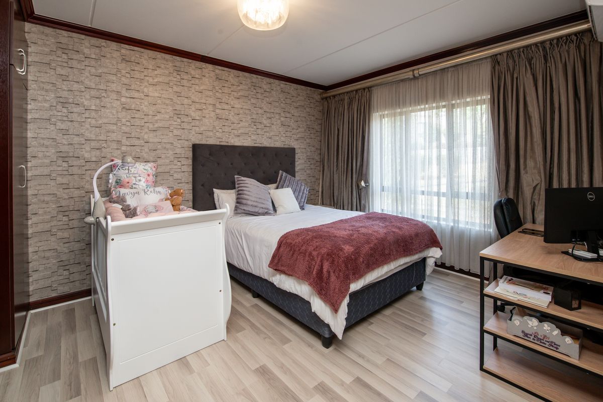 A well-maintained bedroom featuring laminate flooring, textured accent wallpaper, and large windows with curtain tracks, providing a comfortable and functional living space.