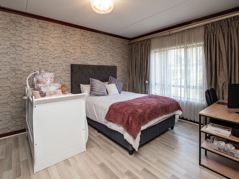 A well-maintained bedroom featuring laminate flooring, textured accent wallpaper, and large windows with curtain tracks, providing a comfortable and functional living space.