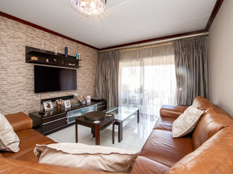 A well-maintained living room featuring a textured accent wall, built-in shelving, tiled flooring, and large sliding glass doors providing natural light.