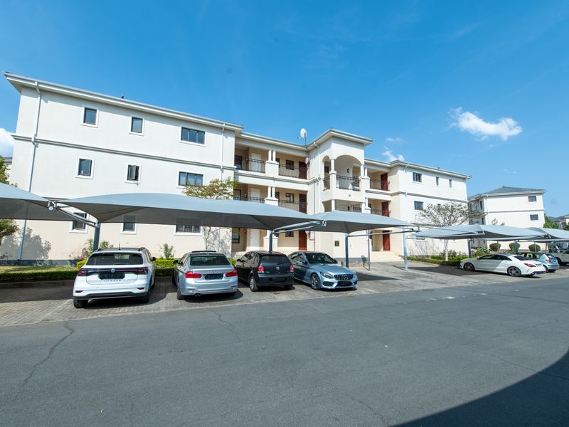Exterior view of a multi-story apartment complex featuring covered parking bays and private balconies for residents.