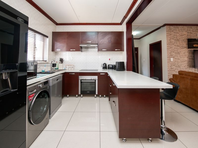 Modern kitchen featuring dark wood cabinetry, stone countertops, integrated oven and hob, and a breakfast bar, seamlessly flowing into the adjacent living area.