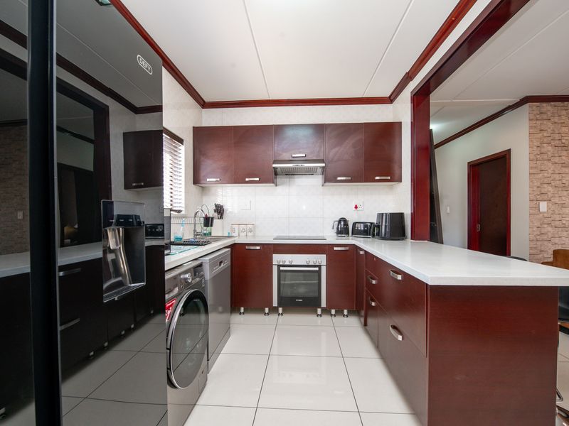 Modern kitchen featuring dark wood cabinetry, stone countertops, integrated appliances, and tiled flooring, offering a clean and functional workspace.