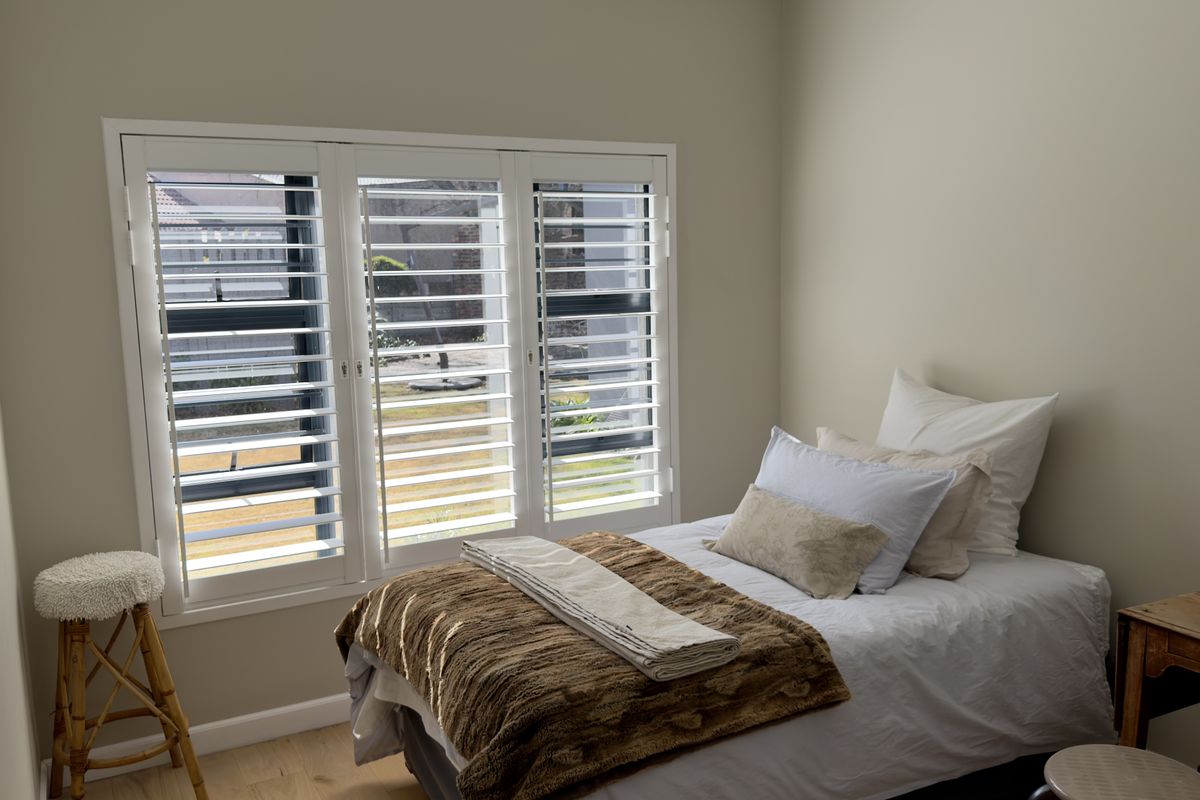 A bright bedroom featuring light timber flooring and white plantation shutters, offering a clean and neutral aesthetic.