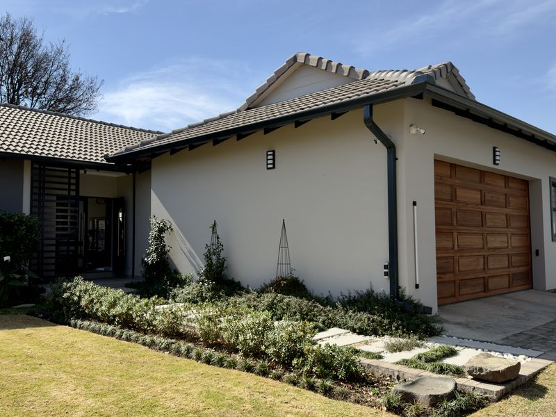 A well-maintained front exterior view of the house featuring a tiled roof, a wooden garage door, and a neatly landscaped garden.