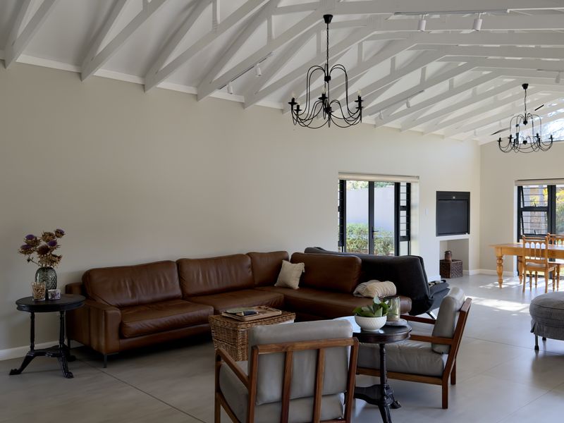 Spacious open-plan living and dining area featuring a high vaulted ceiling with exposed rafters, tiled flooring, and large windows providing natural light.