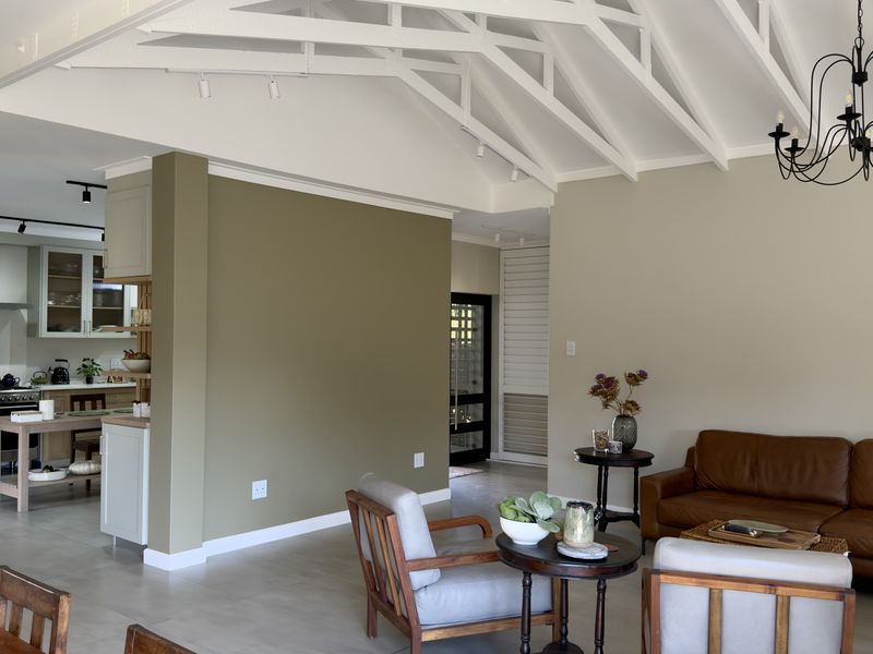 Spacious open-plan living area featuring a vaulted ceiling with exposed rafters, modern kitchen with built-in cabinetry, and neutral tiled flooring throughout.