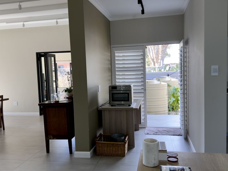 Open plan living area featuring tiled floors, modern track lighting, and plantation shutters, with seamless access to the outdoor patio area.