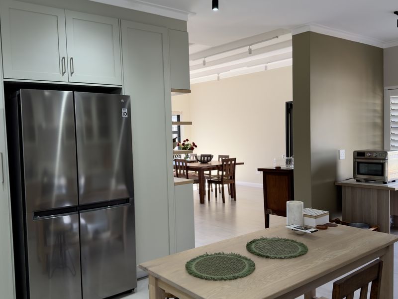 An open-plan living and kitchen area featuring modern cabinetry, neutral tones, and natural light flowing through louvre shutters.