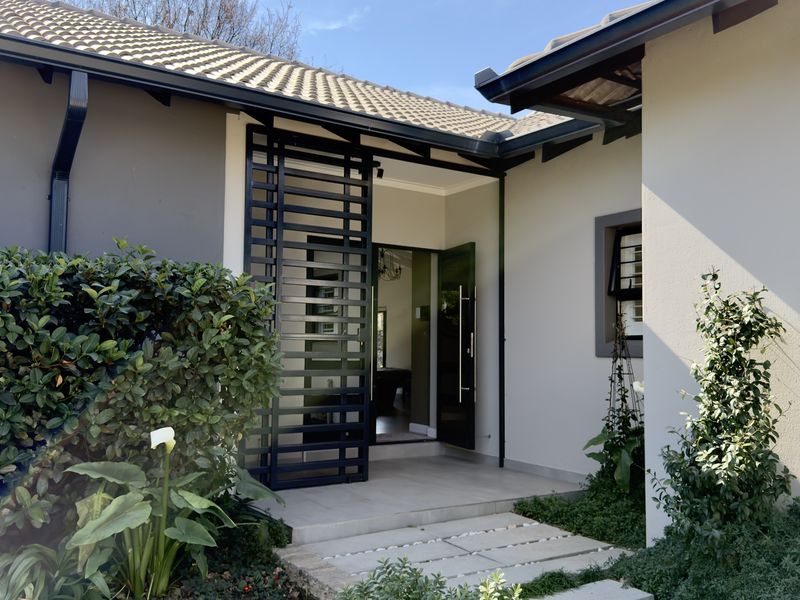 A well-maintained front entrance featuring a modern security gate, tiled roof, and a paved walkway leading to the main door.