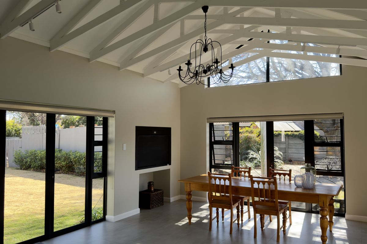 Spacious living area featuring a high vaulted ceiling with exposed trusses, large black-framed windows, and a built-in fireplace, offering abundant natural light.