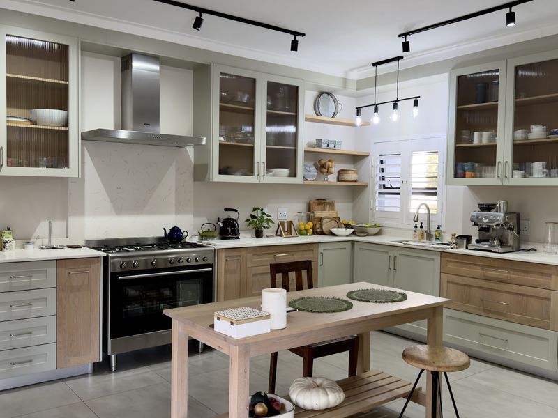 Modern kitchen featuring sage green and wood-tone cabinetry, stone countertops, a gas range with stainless steel extractor, and stylish fluted glass display cabinets.