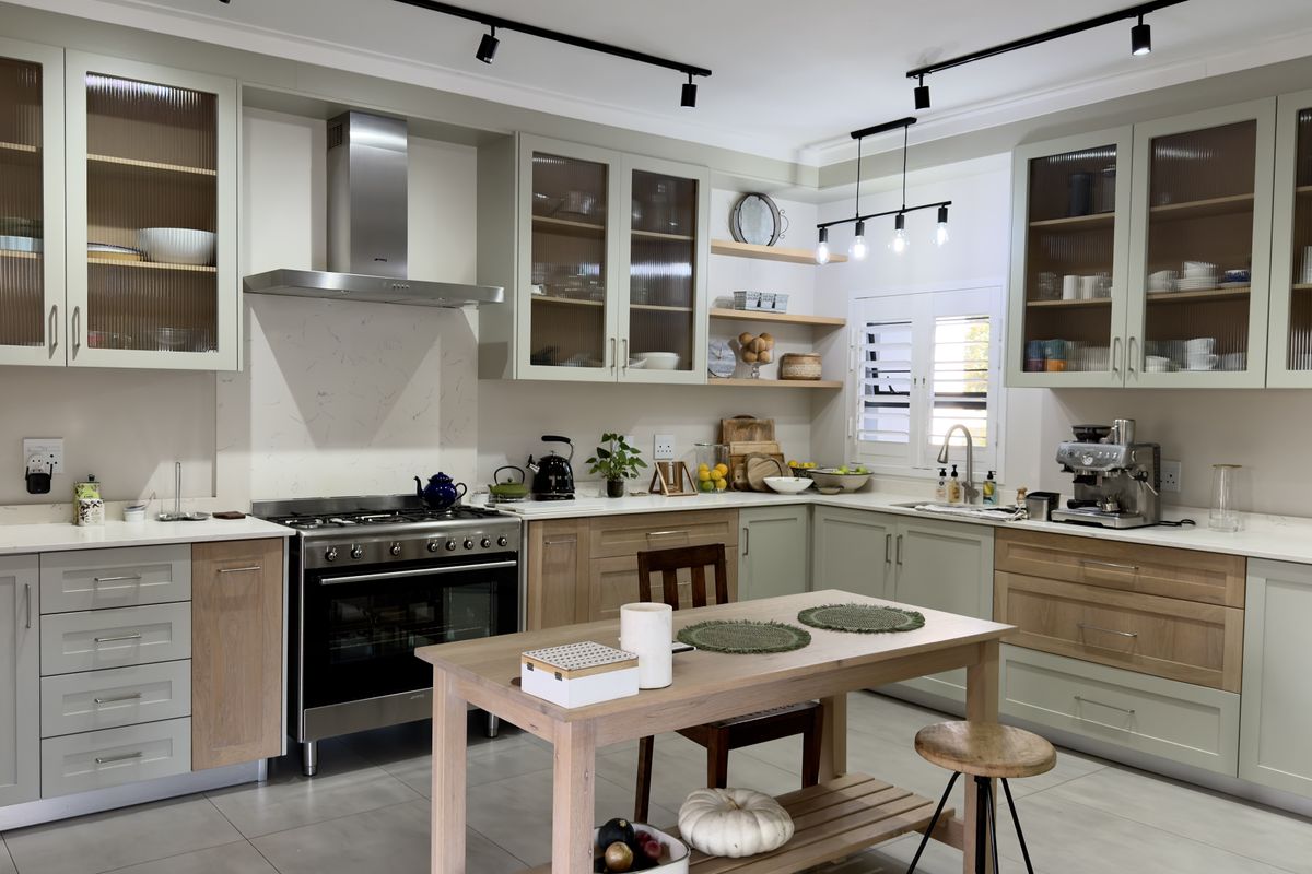Modern kitchen featuring sage green and wood-tone cabinetry, stone countertops, a gas range with stainless steel extractor, and stylish fluted glass display cabinets.