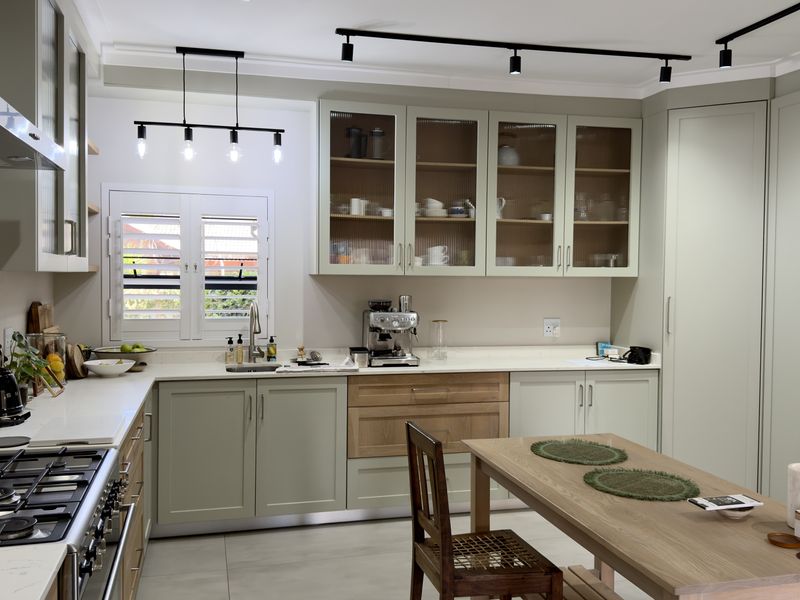 Modern kitchen featuring sage green cabinetry, stone countertops, gas hob, extractor fan, and stylish track lighting with ample storage and a functional layout.
