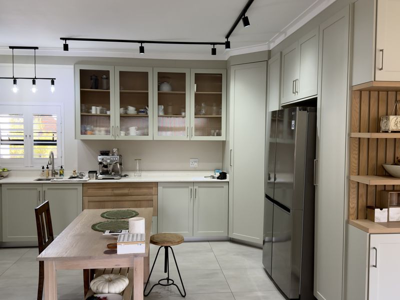 Modern kitchen featuring sage green shaker-style cabinetry, quartz countertops, integrated storage, and stylish track lighting, creating a functional and contemporary culinary space.