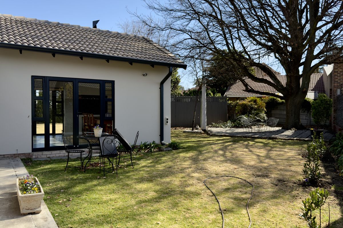 Rear view of the property featuring a well-maintained lawn, concrete patio area, and modern dark-framed sliding doors leading into the home.