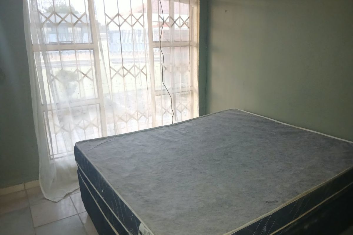 A bedroom featuring tiled flooring and a window fitted with a security gate, requiring cosmetic updates to the wall finishes.