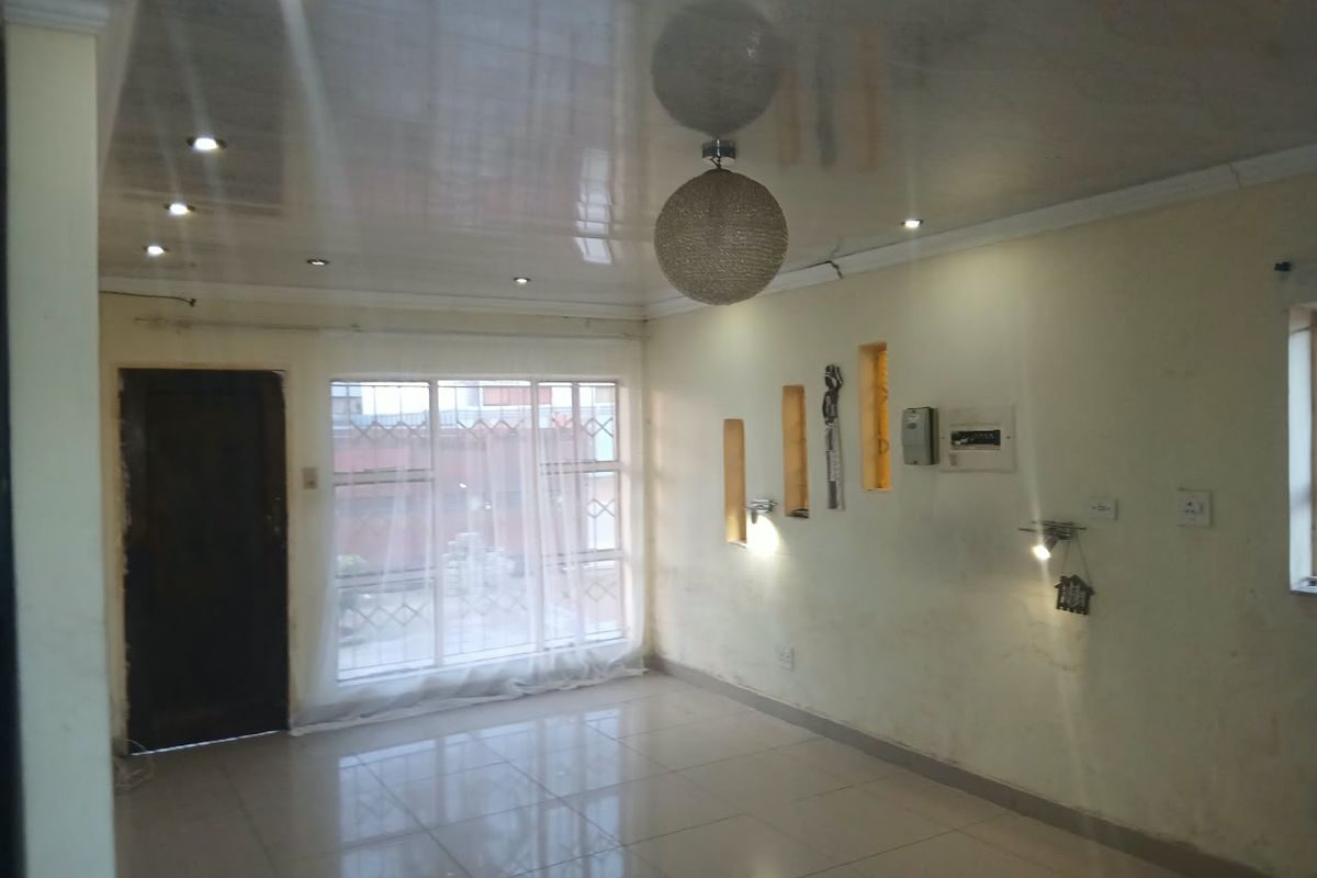 An empty living room featuring glossy ceiling finishes, tiled floors, built-in wall niches, and recessed lighting, requiring minor cosmetic wall repairs.