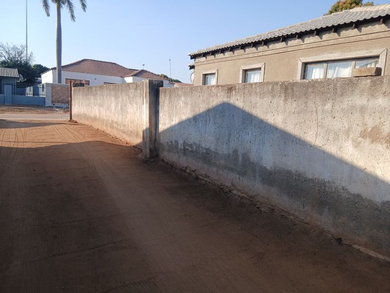 View of the property exterior featuring a perimeter boundary wall and unpaved driveway area.