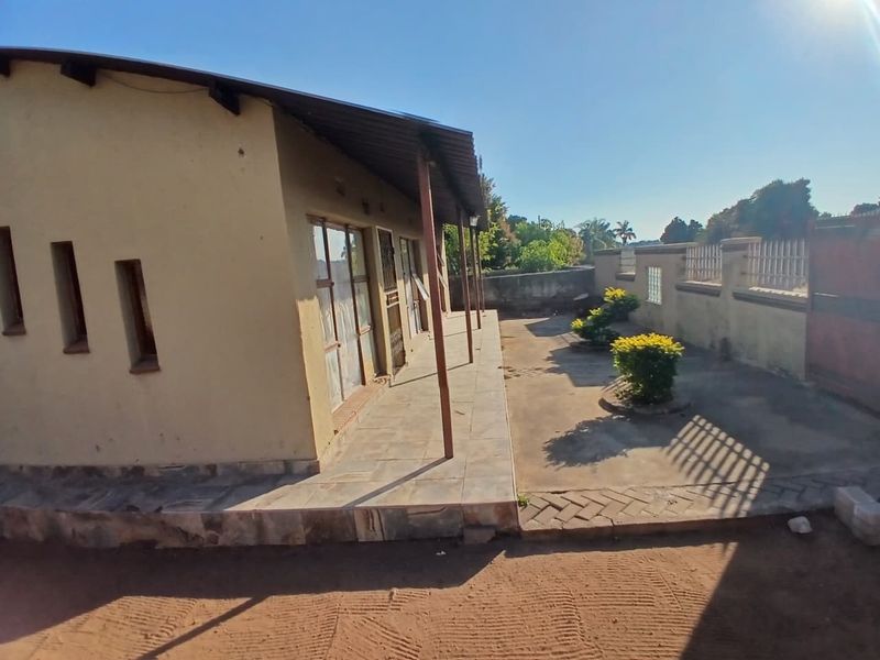Rear view of the property featuring a covered patio area, tiled flooring, and a surrounding perimeter wall with paved garden space.