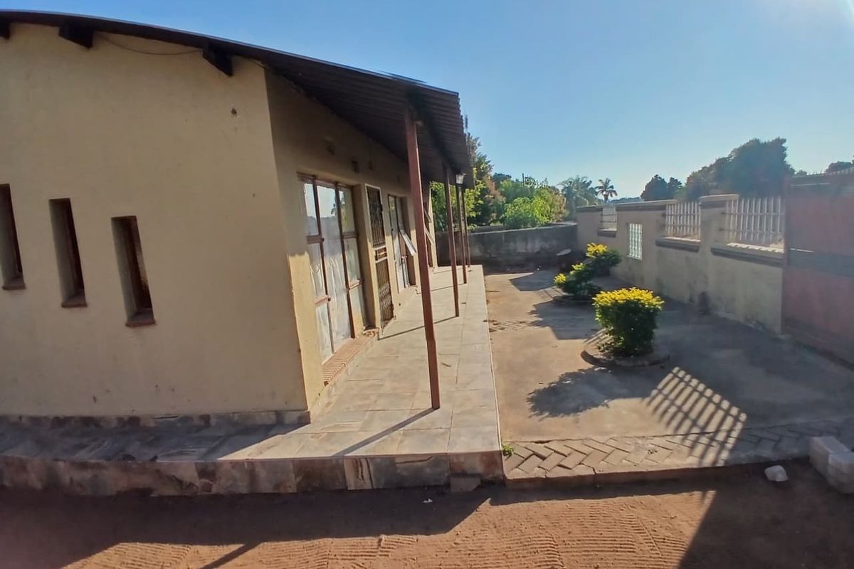 Rear view of the property featuring a covered patio area, tiled flooring, and a surrounding perimeter wall with paved garden space.