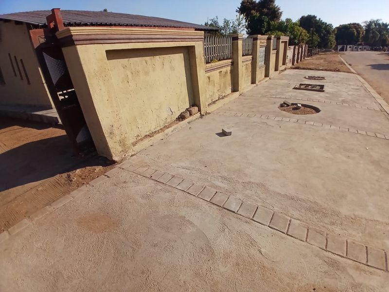 Exterior view of the property frontage featuring a concrete driveway and a perimeter boundary wall with metal fencing.
