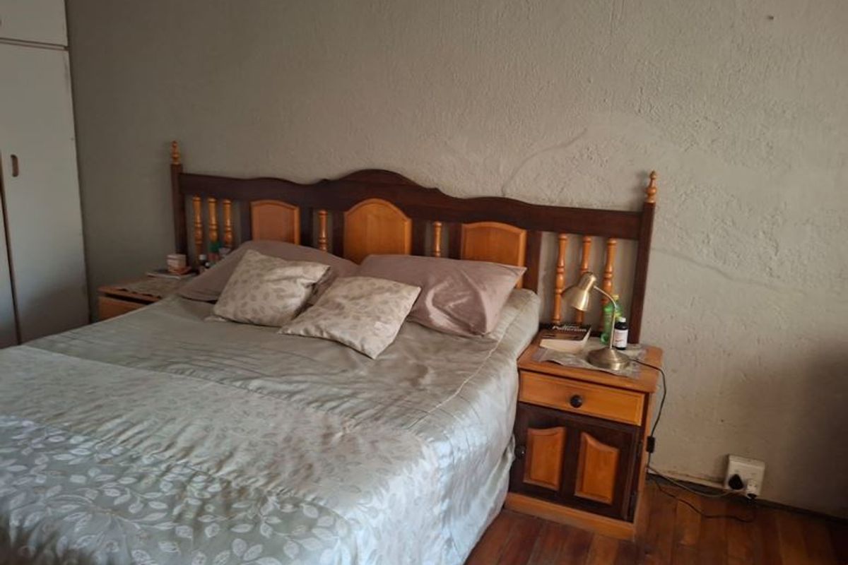 A bedroom featuring timber flooring and a built-in wardrobe, showing visible signs of wear including cracked wall plaster.