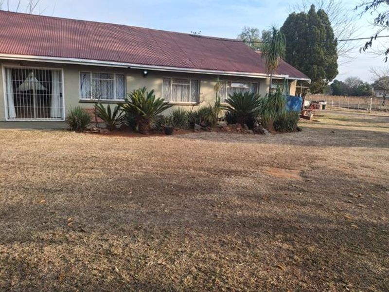 Rear view of the house featuring a corrugated metal roof, security bars on windows, and a sliding glass door leading to the garden area.