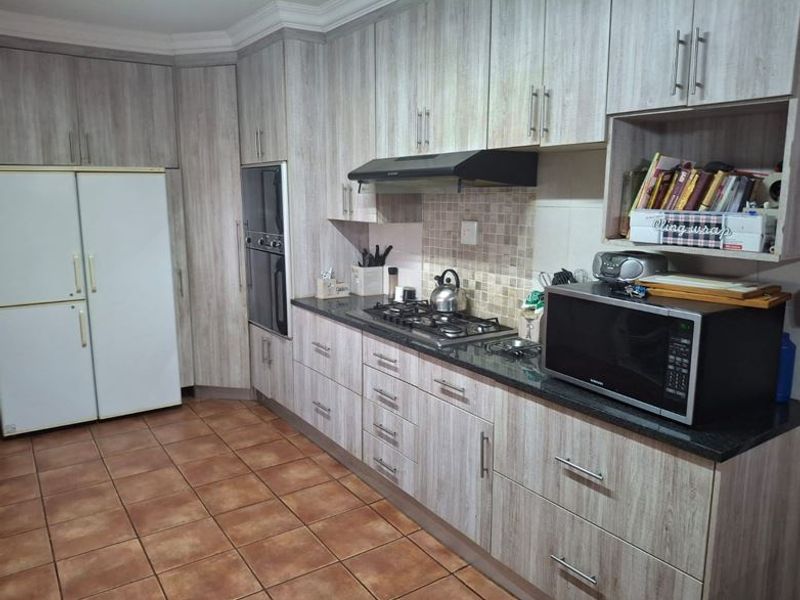 A functional kitchen featuring light wood-grain cabinetry, granite countertops, a gas hob with extractor fan, and a built-in oven with tiled flooring.