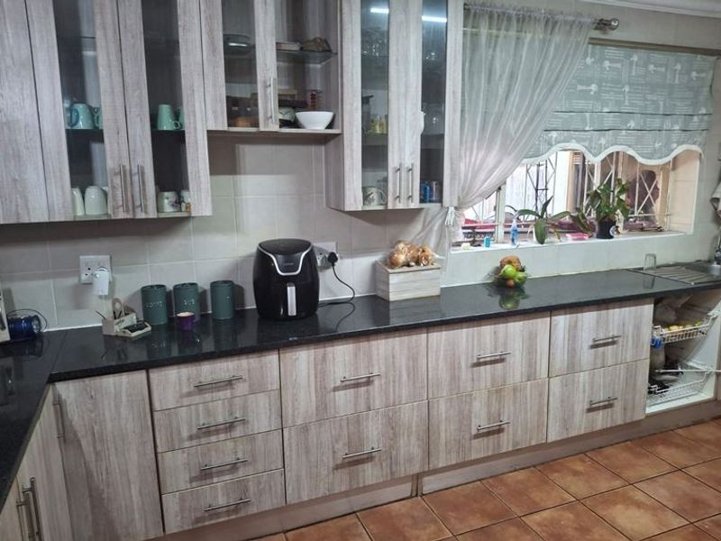 A functional kitchen featuring light wood-grain laminate cabinetry, dark granite countertops, and tiled flooring with a window overlooking the exterior.