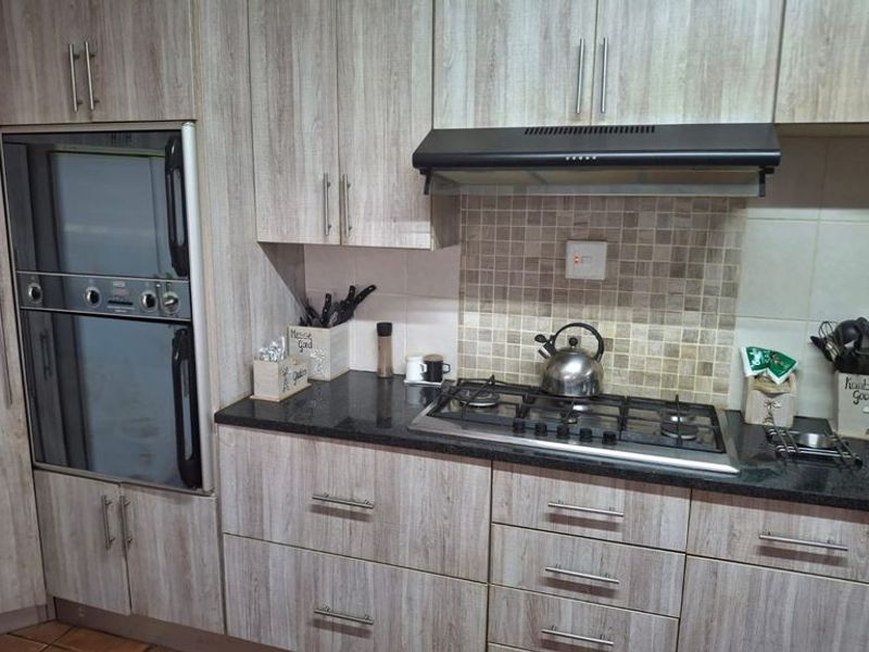 A functional kitchen featuring wood-look laminate cabinetry, granite countertops, a built-in oven, and a gas hob with a tiled backsplash.
