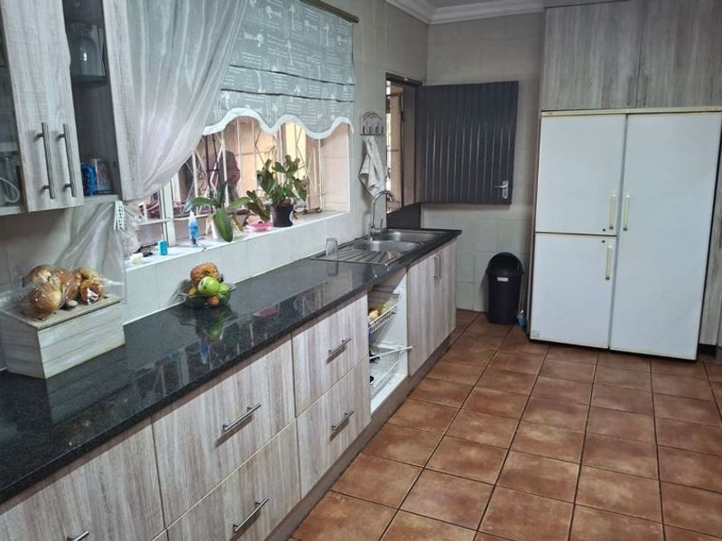 A functional kitchen featuring granite countertops, ample built-in cabinetry, a double sink, and tiled flooring with security bars on the window.