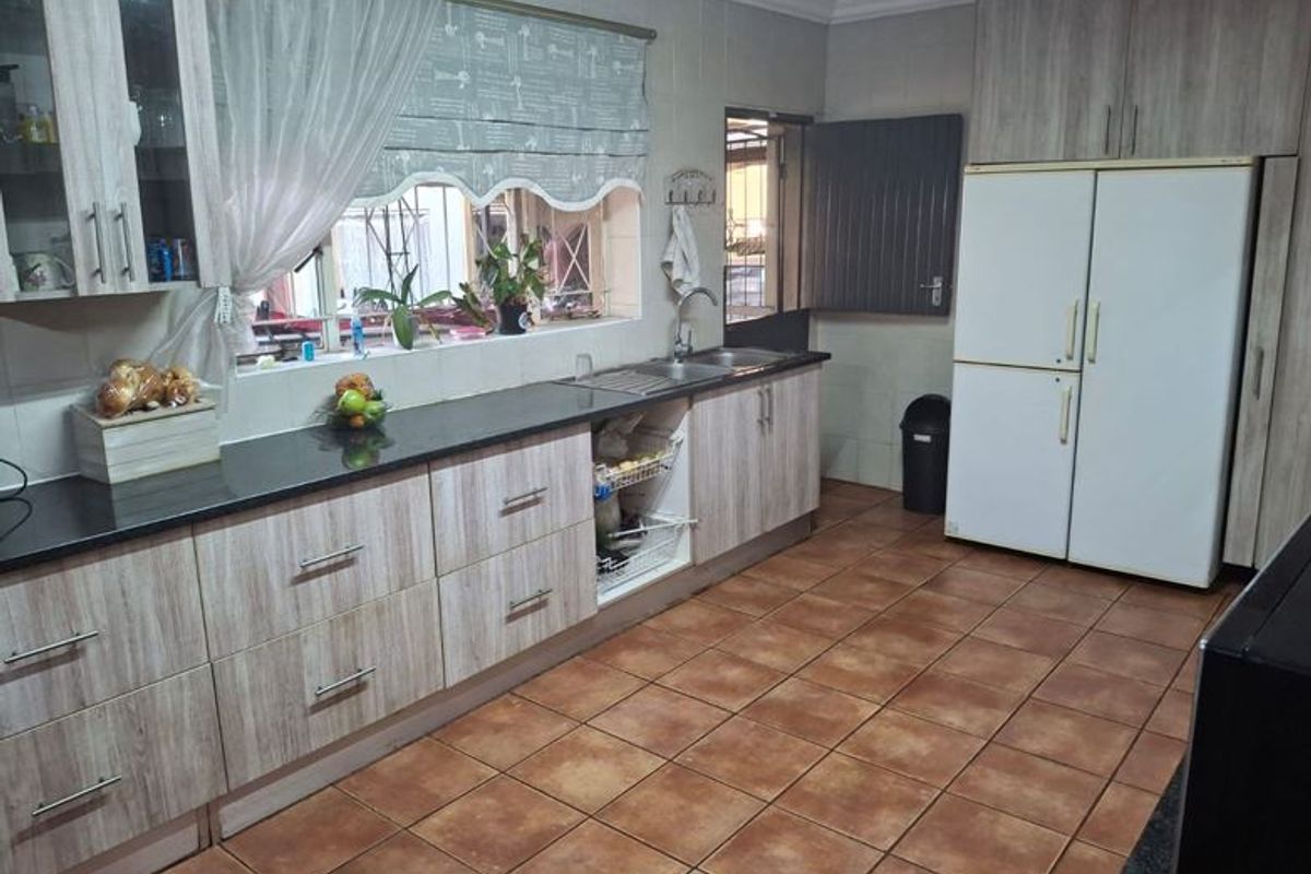 A functional kitchen featuring wood-look cabinetry, granite countertops, a double sink, and durable tiled flooring with ample storage space.