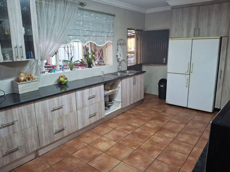 A functional kitchen featuring wood-look cabinetry, granite countertops, a double sink, and durable tiled flooring with ample storage space.