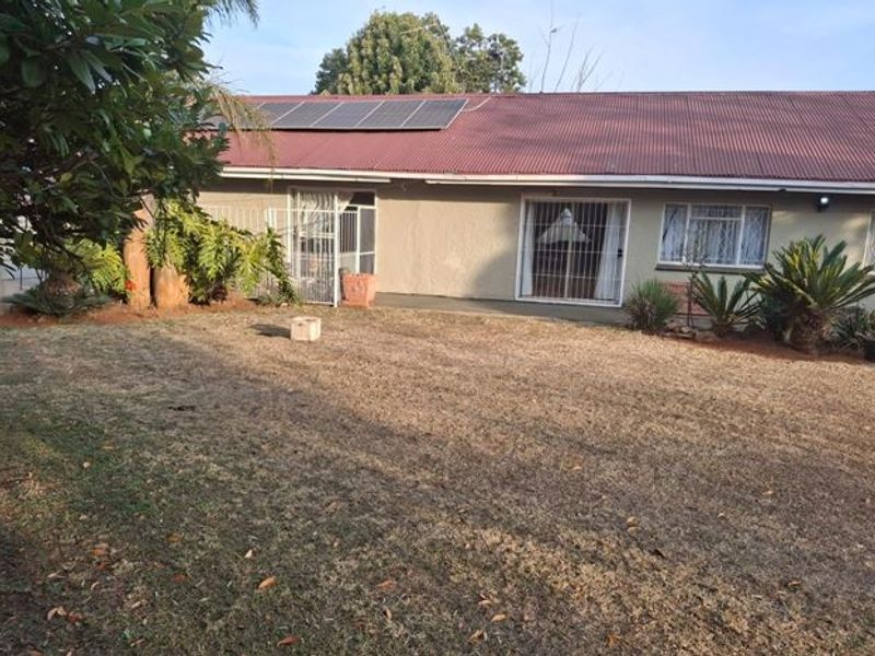Rear view of the house featuring a corrugated metal roof with solar panels, security gates, and sliding doors leading to the garden.