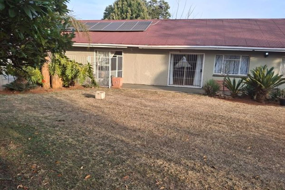 Rear view of the house featuring a corrugated metal roof with solar panels, security gates, and sliding doors leading to the garden.