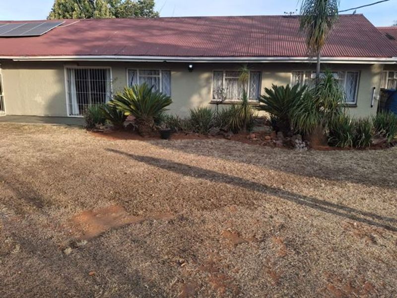 Rear view of a single-story house featuring a corrugated metal roof with solar panels, security-barred windows, and a landscaped garden area.