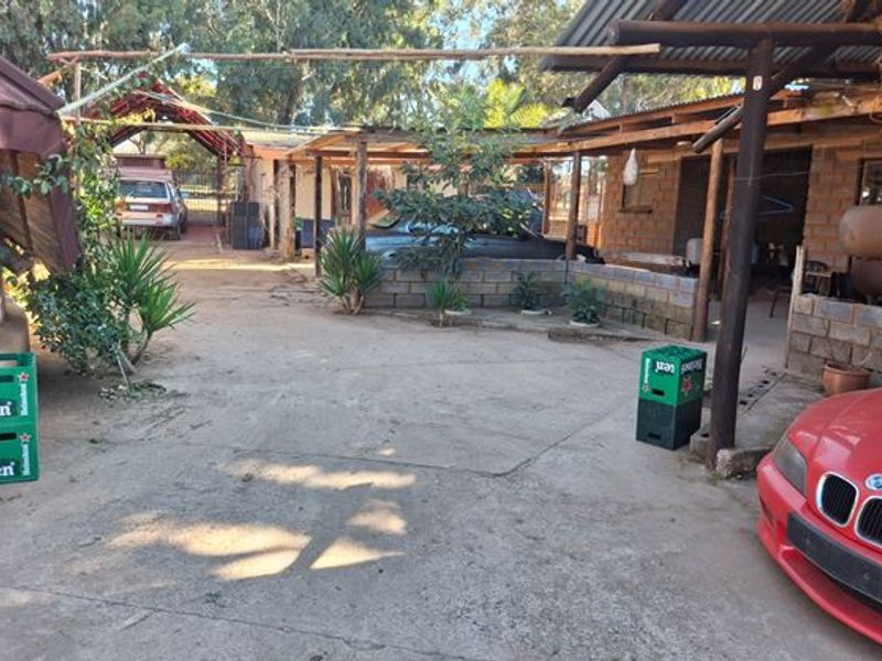 A rustic outdoor area featuring a concrete driveway, covered patio space with timber supports, and brick walling, suitable for farm-style utility or parking.
