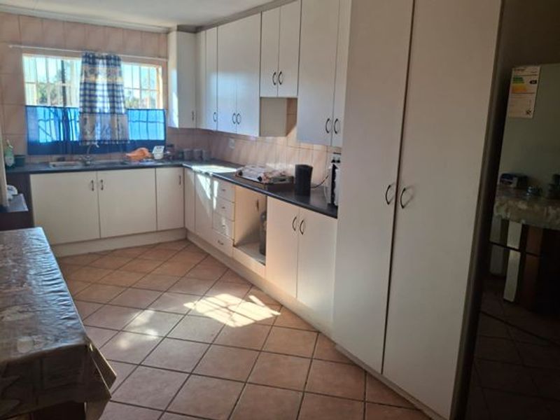 Functional kitchen featuring ample built-in cabinetry, laminate countertops, double basin sink, and tiled flooring with natural light from a window with security bars.