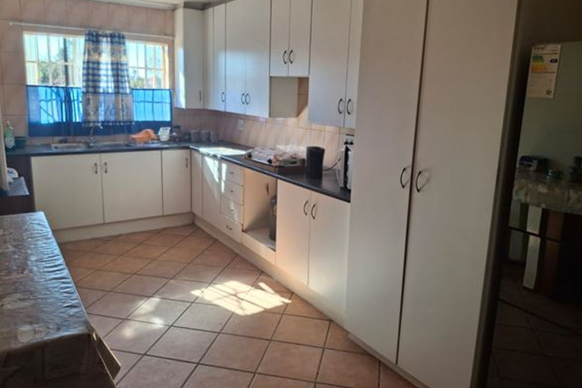 Functional kitchen featuring ample built-in cabinetry, laminate countertops, double basin sink, and tiled flooring with natural light from a window with security bars.