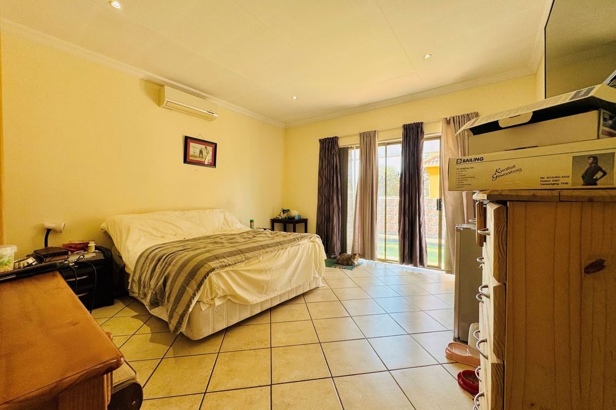 Spacious bedroom featuring tiled flooring, a wall-mounted air conditioning unit, and sliding glass doors providing direct access to the outdoor area.