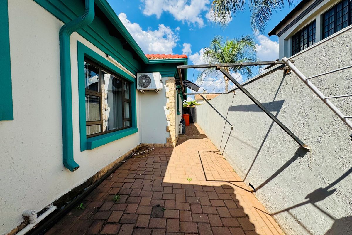 A side exterior walkway featuring paved flooring, a wall-mounted air conditioning unit, and a fixed metal washing line structure.