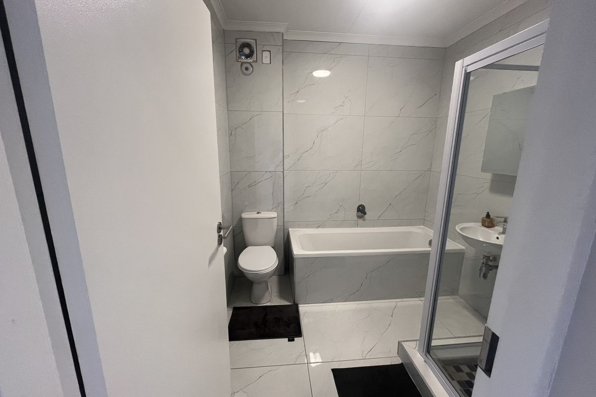 A modern bathroom featuring marble-look wall and floor tiles, a built-in bathtub, a separate shower enclosure, and a wall-mounted extractor fan.