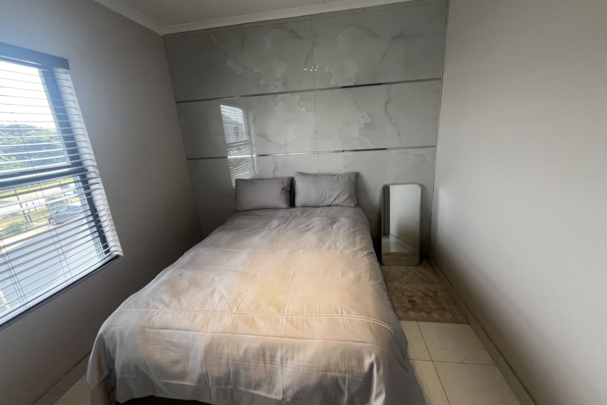A modern bedroom featuring large format marble-effect wall tiling as a feature headboard and sleek floor tiles.