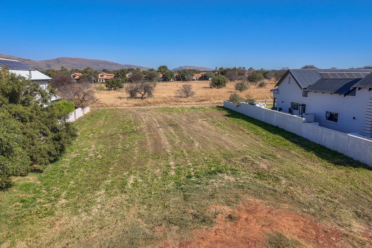 An aerial view of a vacant residential plot situated between existing homes, featuring clear boundaries and open space ready for development.