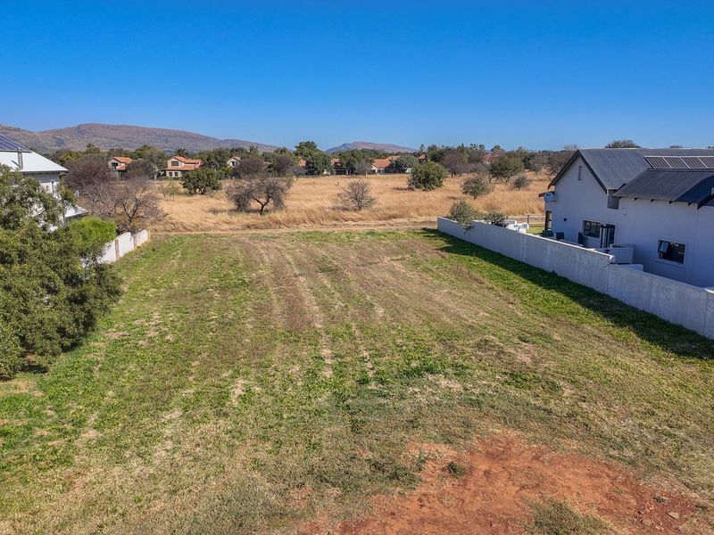 An aerial view of a vacant residential plot situated between existing homes, featuring clear boundaries and open space ready for development.